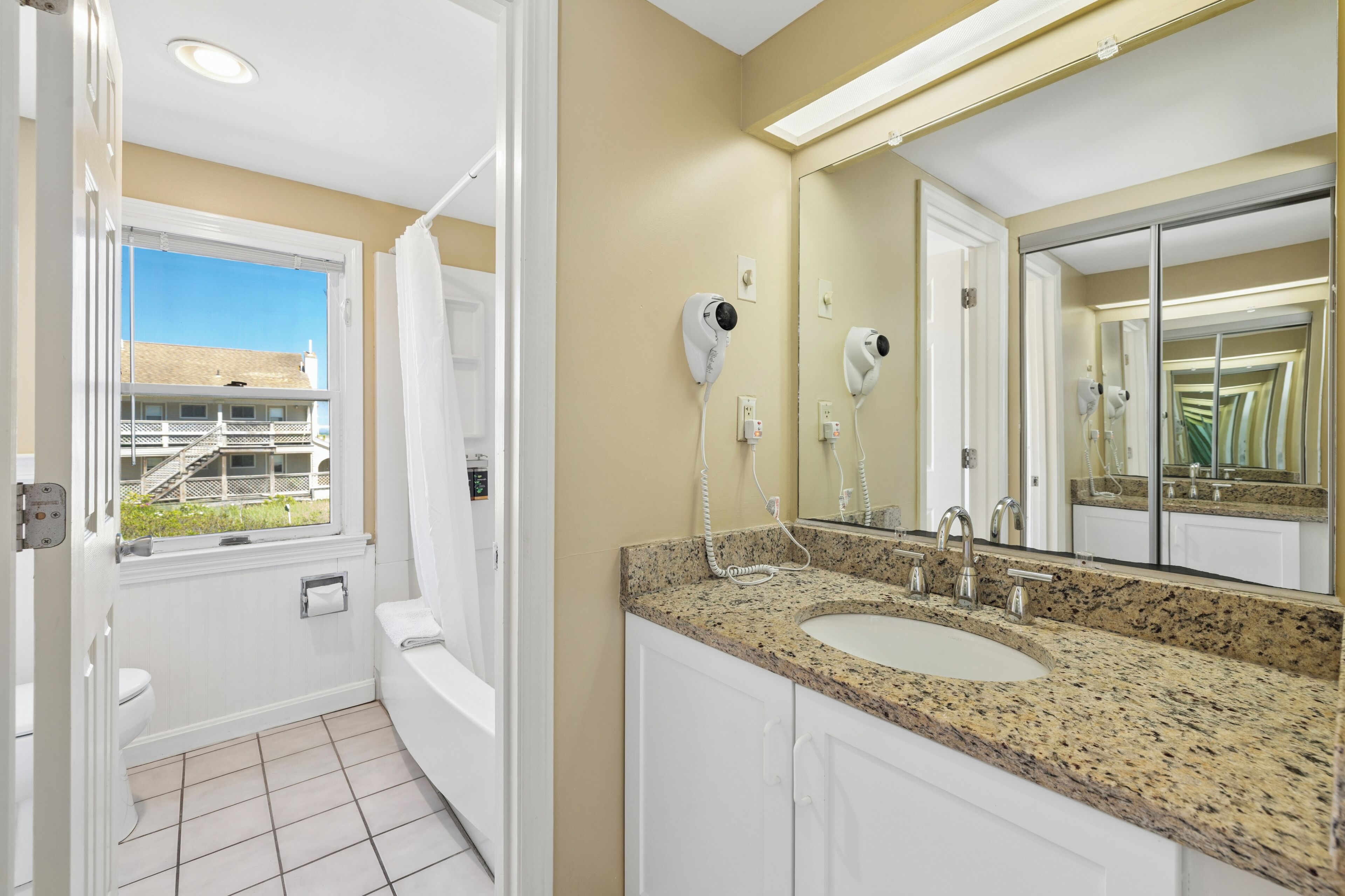 A bathroom with a window, a sink, a mirror, and a hairdryer.