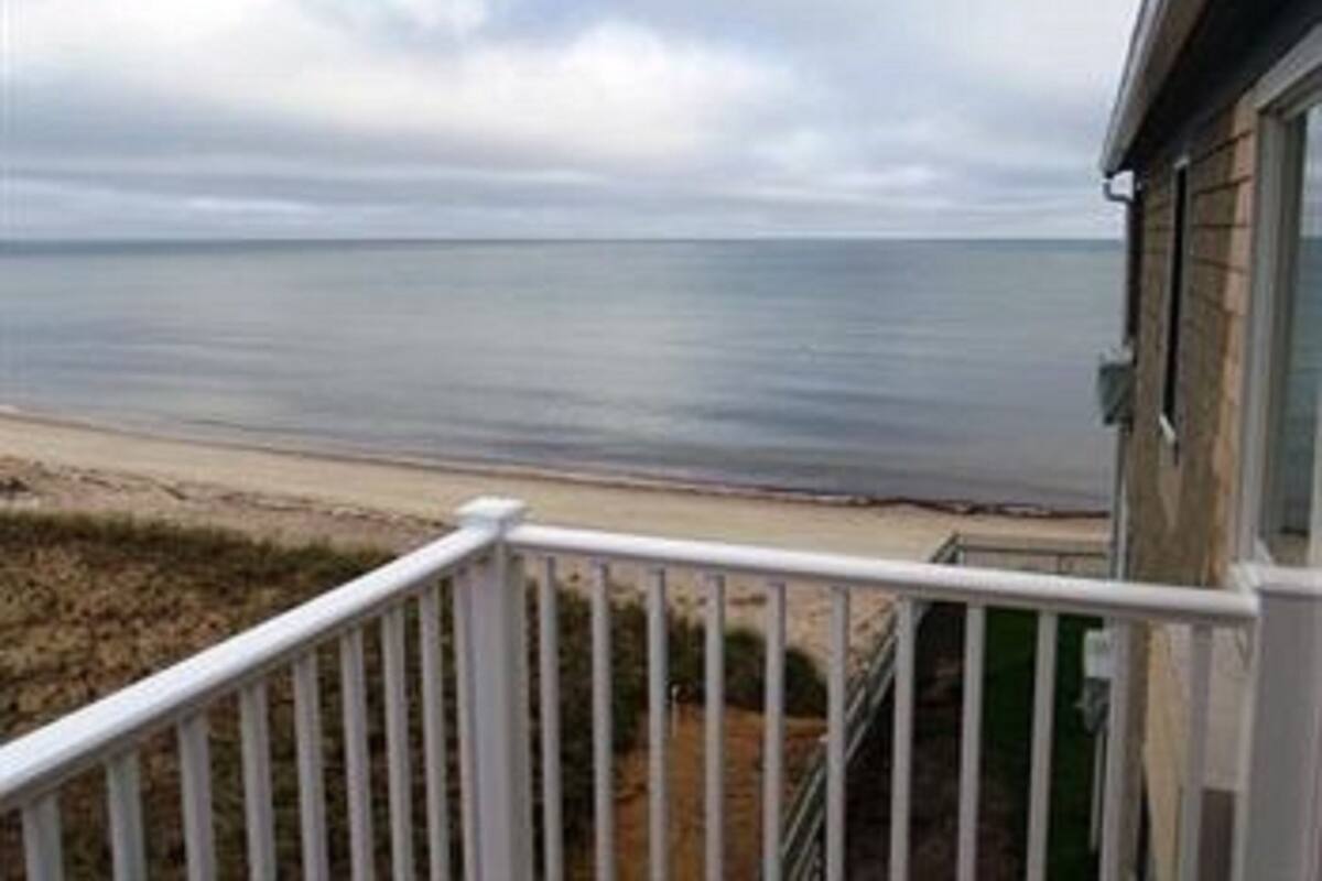 A beach view from a balcony with a railing, overlooking the ocean.