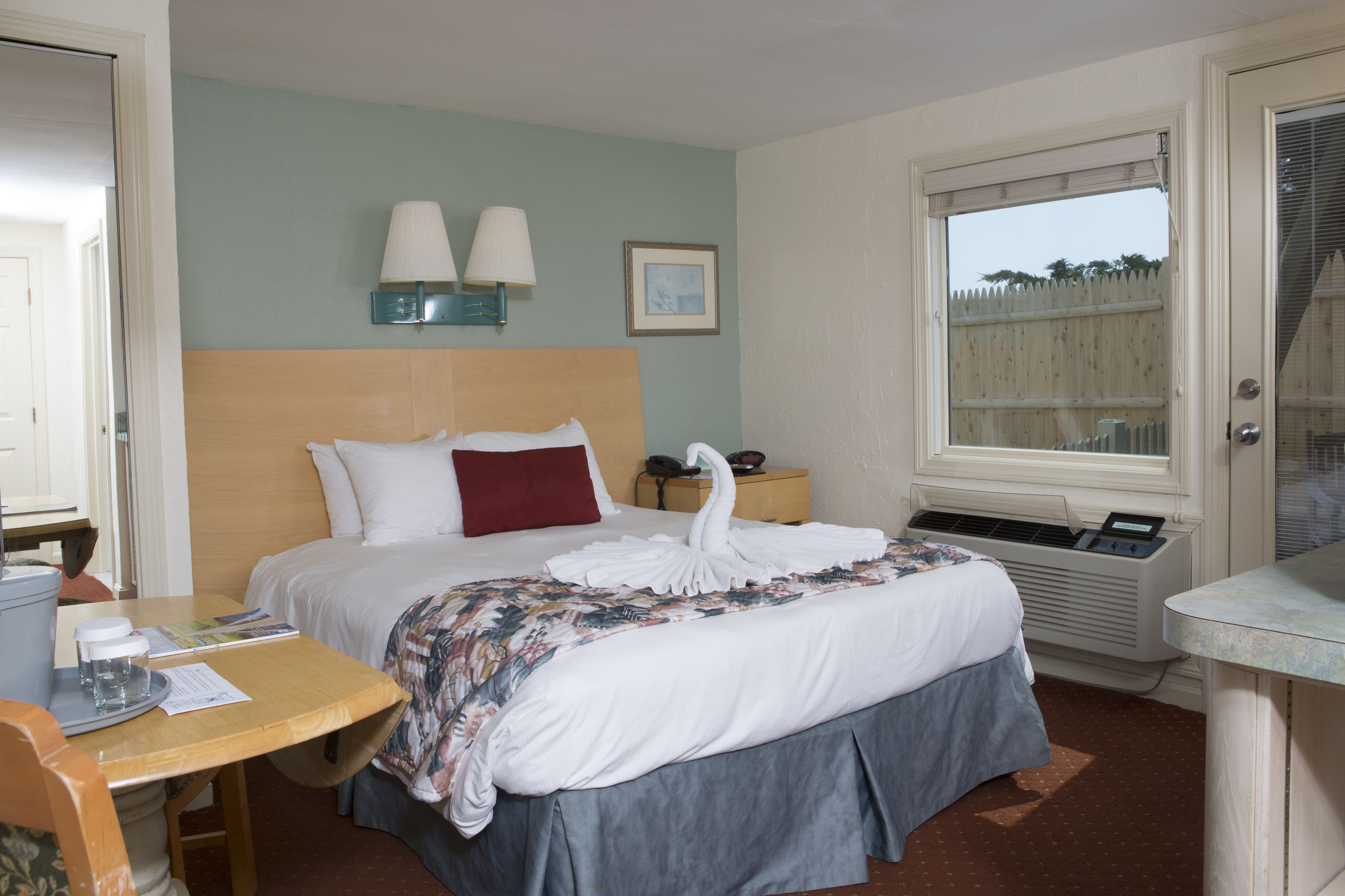 A hotel room with a bed, bedside lamps, a window, and a desk with a chair.