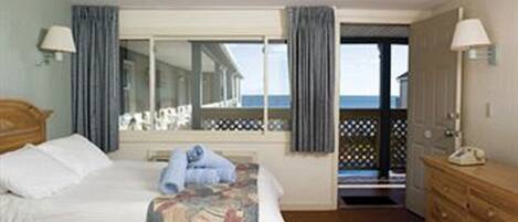 Ein Hotelzimmer mit Bett, Schminktisch, einem Fenster mit Vorhängen und Blick aufs Meer.
