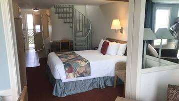 A hotel room with a bed, a chair, a desk, a lamp, and a staircase.