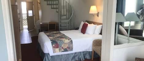 Una habitación de hotel con cama, una silla, un escritorio, una lámpara y una escalera.