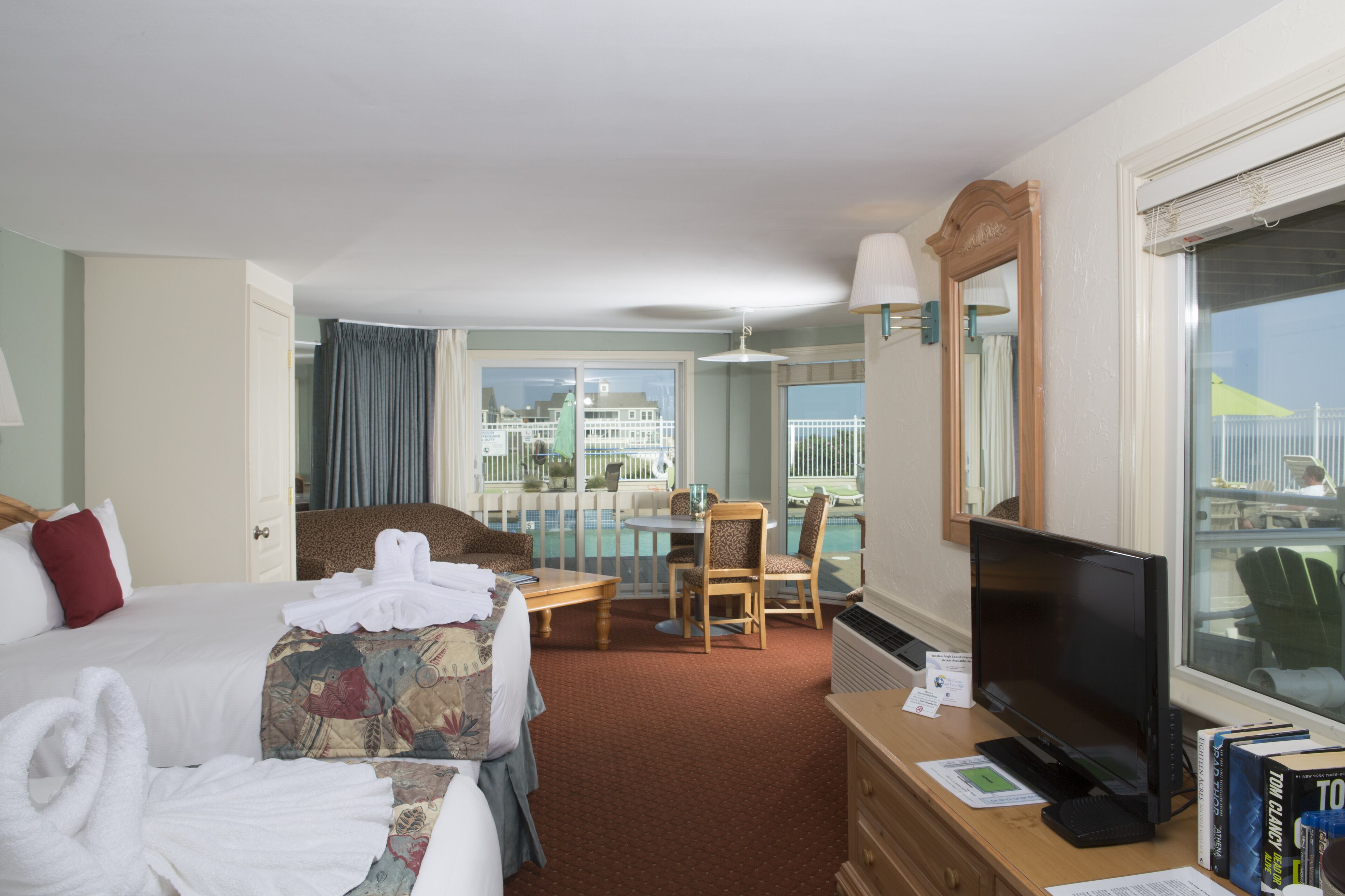 A hotel room with a bed, a desk with a computer, a TV, and a balcony with a view of the city.