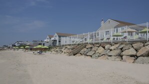 Ein Haus am Strand mit weißem Zaun, einer Treppe, die zu einem Balkon führt, und einem Sandstrand.