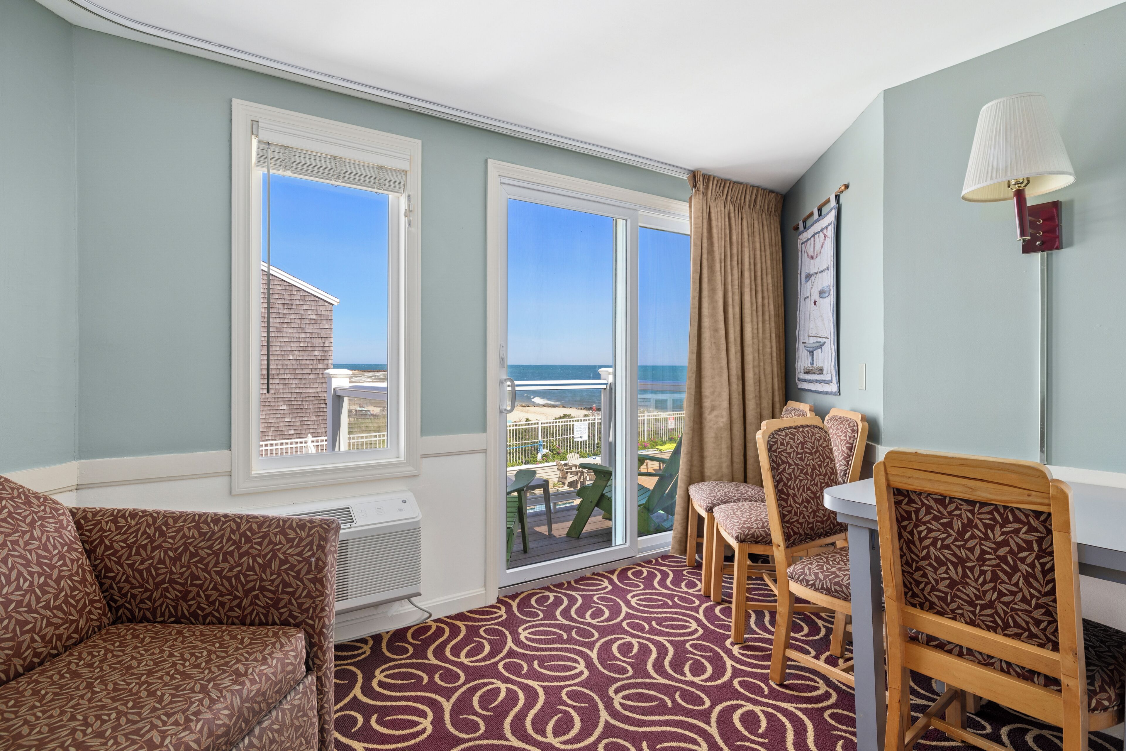 A room with a patterned carpet, a sofa, two chairs, a table, and a lamp.