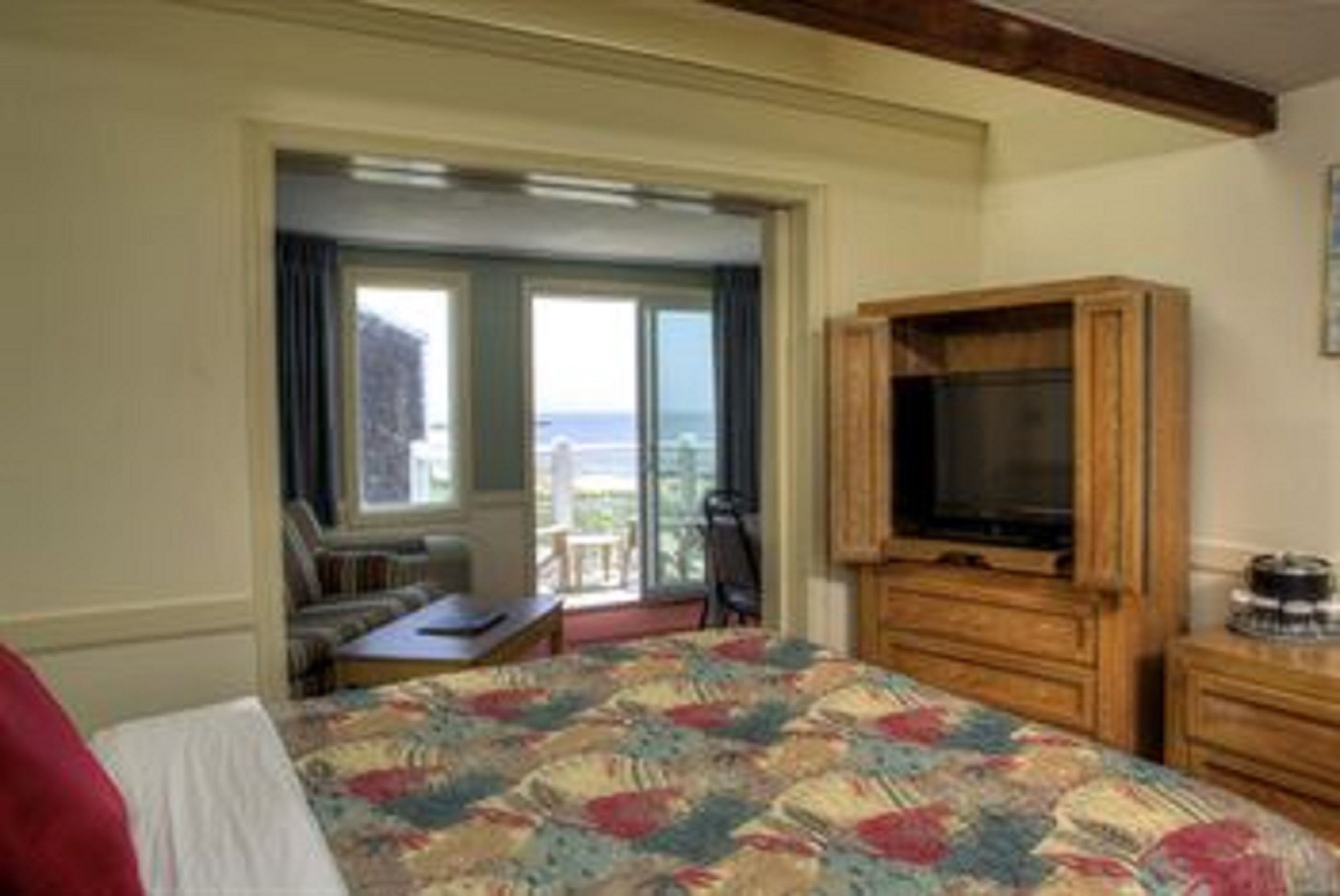 Habitación de hotel con cama, televisor, aparador de madera y balcón con vista al mar.