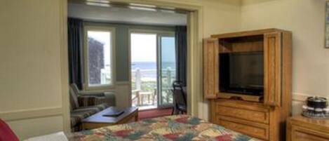 A hotel room with a bed, a television, a wooden cabinet, and a balcony with a view of the sea.