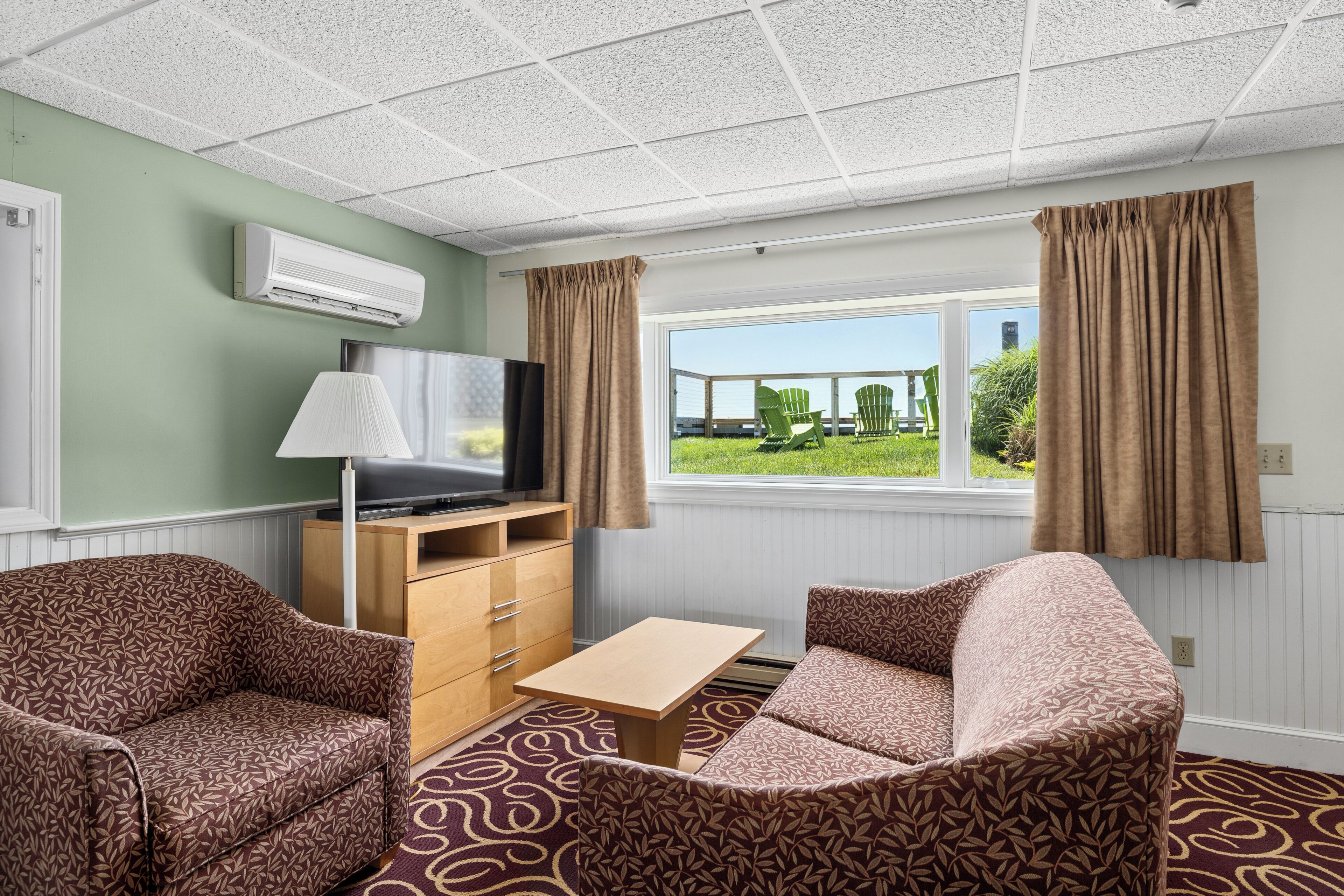 A room with a sofa, a small table, a TV, and a window with curtains.