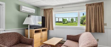 Ein Zimmer mit einer Couch, einem kleinen Tisch, einem Fernseher und einem Fenster mit Vorhängen.