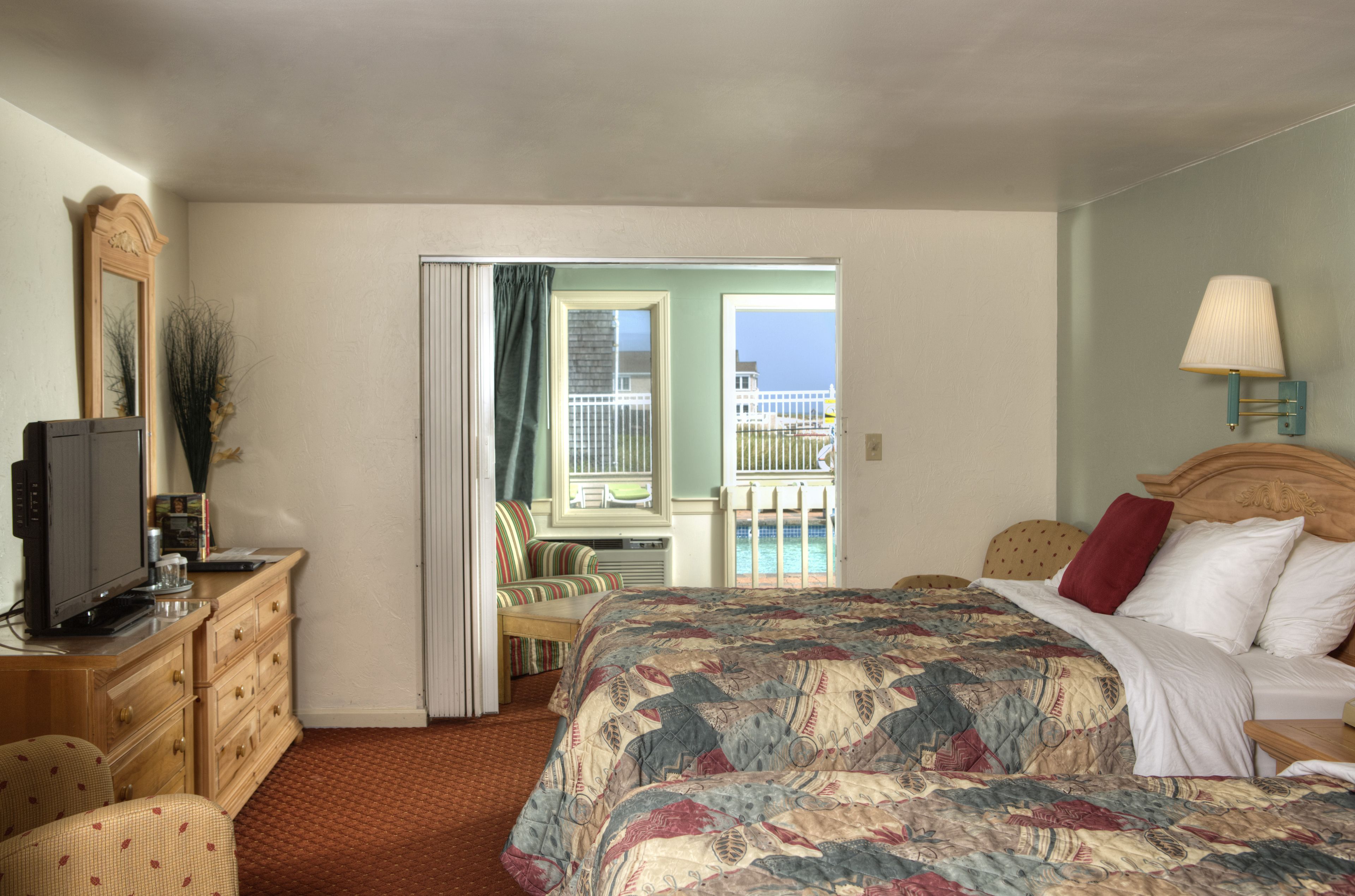 Une chambre d’hôtel comprenant un lit, une télévision, une commode, une chaise et un balcon avec vue sur l’océan.