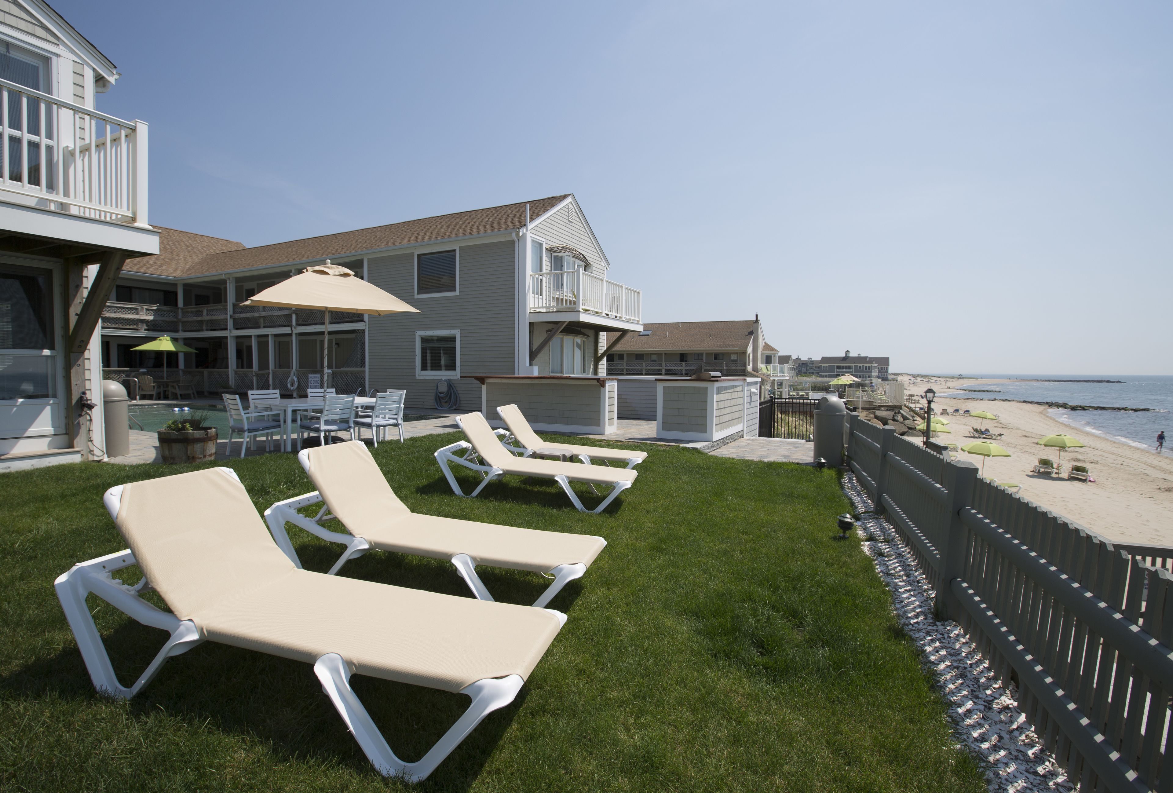 A beachfront property with a pool area, lounge chairs, and a view of the beach.