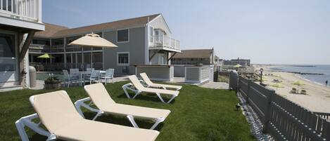 A beachfront property with a pool area, lounge chairs, and a view of the beach.