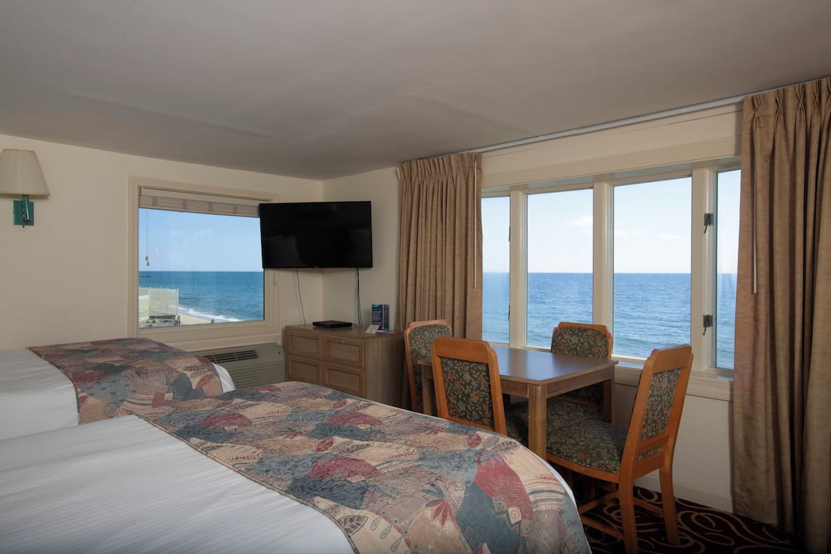 A hotel room with a large bed, a desk, two chairs, a television, and a view of the sea.
