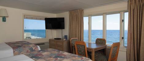 A hotel room with a large bed, a desk, two chairs, a television, and a view of the sea.