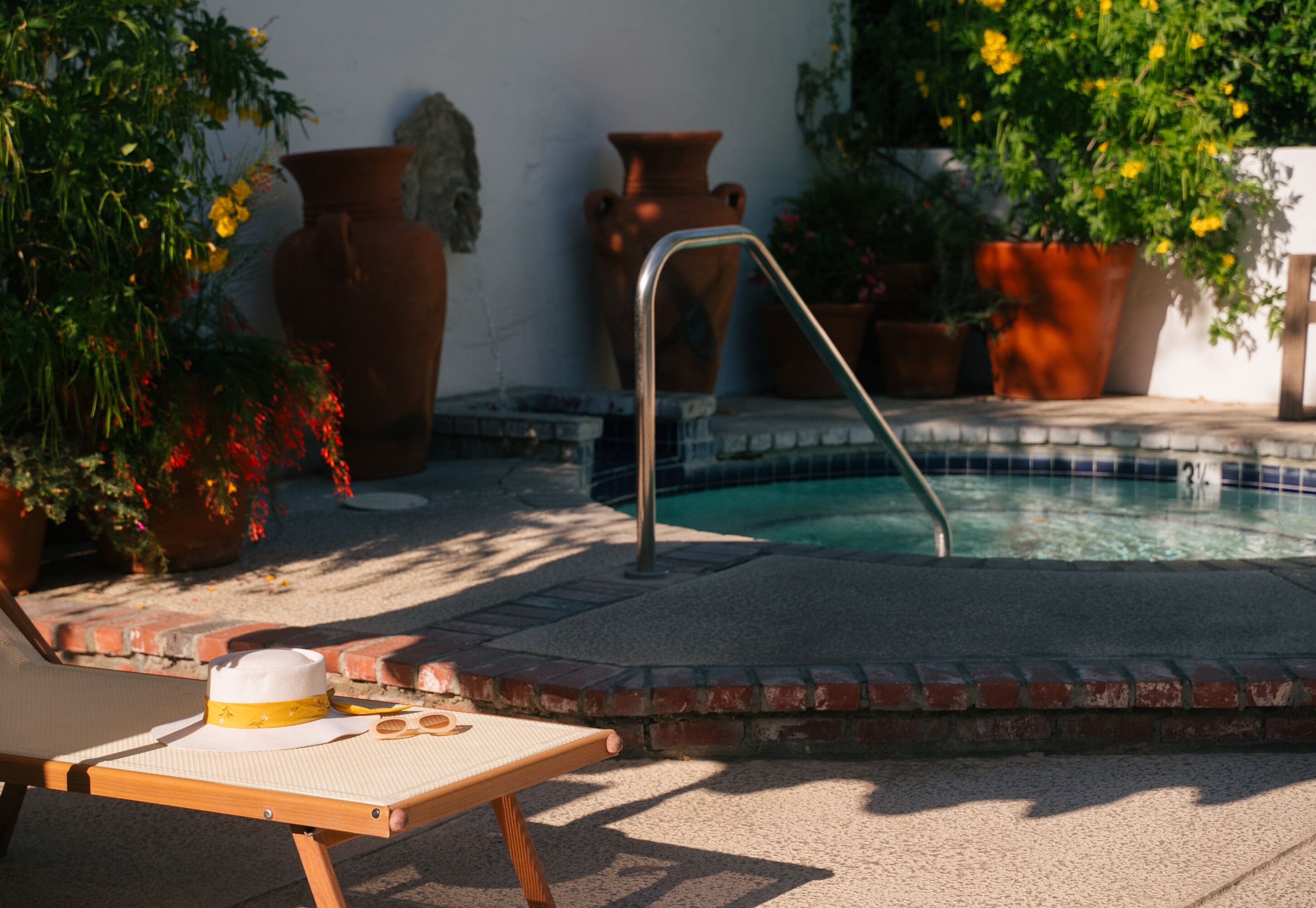 A poolside area with a lounge chair, a hat, and potted plants.