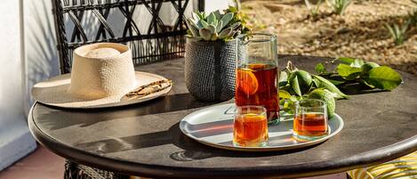 A round table with a pitcher of iced tea, two glasses, a straw, a straw hat, and a woven basket.