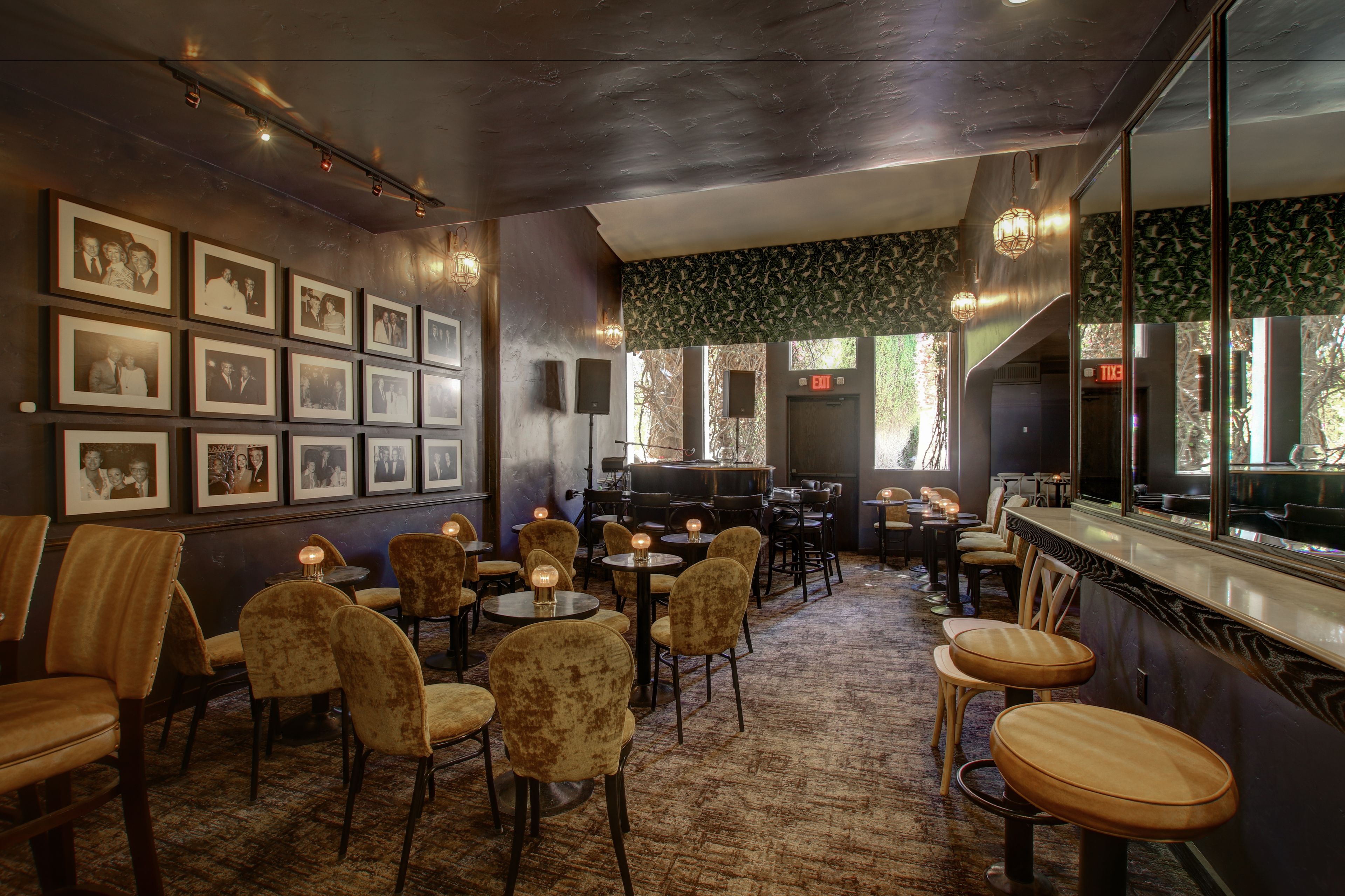 A restaurant with a bar area, multiple tables and chairs, framed pictures on the wall, and a patterned carpet.