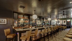 A bar area with multiple stools, a bar counter with a display of bottles, and hanging pendant lights. - Ingleside Estate Hotel & Bungalows- Adults Only (Palm Springs)