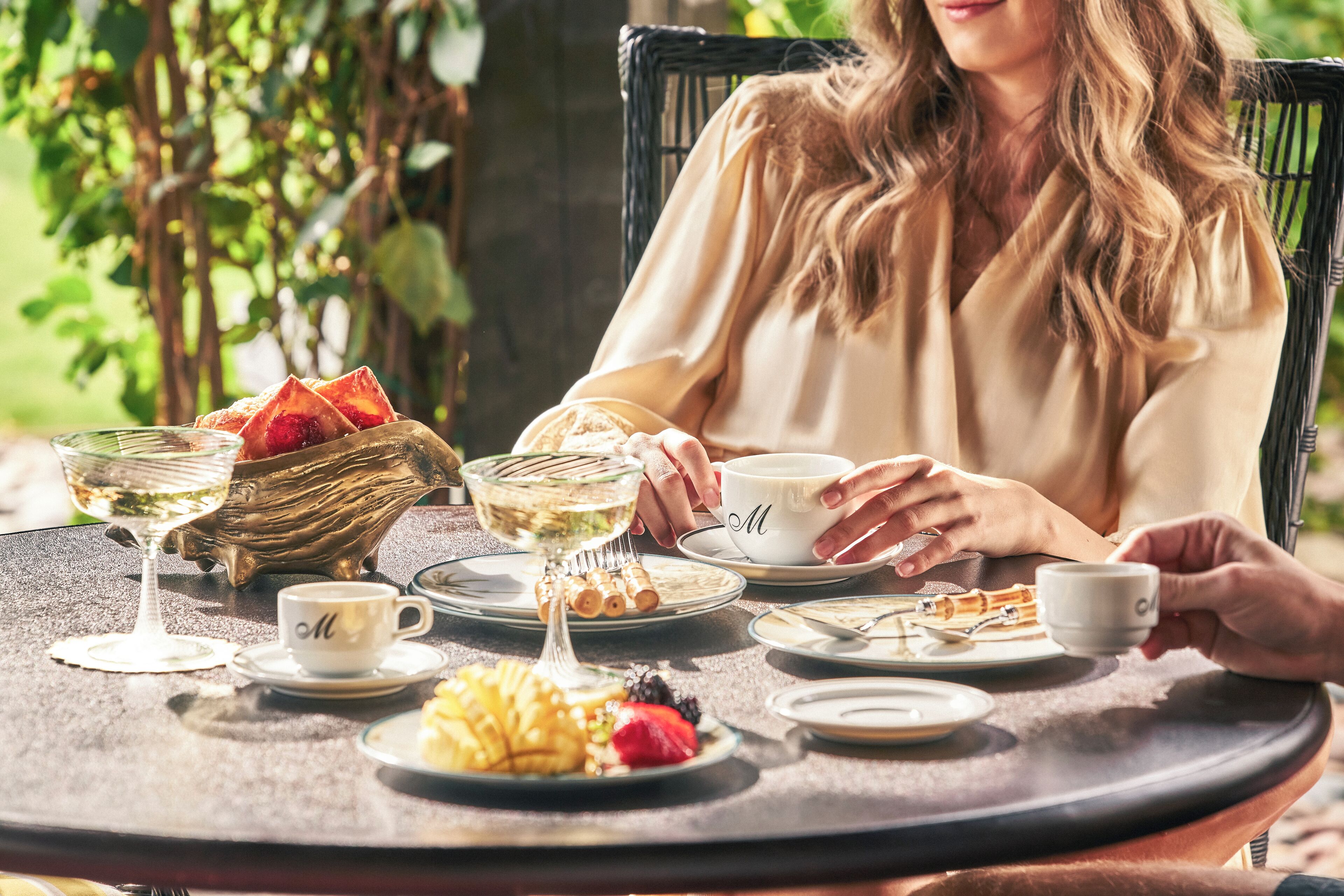 A table set with a glass of white wine, a bowl of fruit, and a cup with a monogrammed saucer.