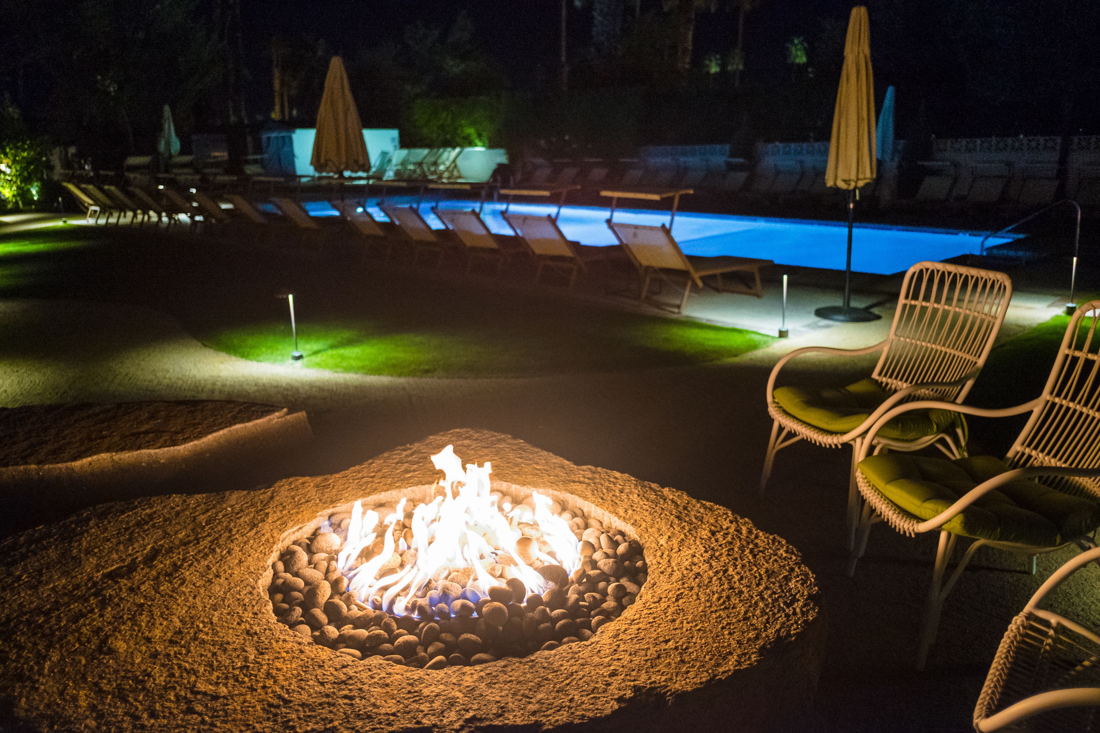 A nighttime outdoor pool area with lounge chairs and a fire pit.