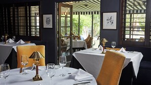 A restaurant with tables set for dining, featuring a view through an open door to an outdoor area. - Ingleside Estate Hotel & Bungalows- Adults Only (Palm Springs)
