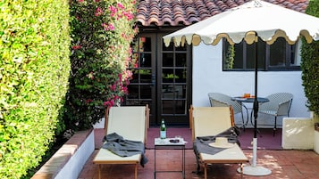 Eine Terrasse mit zwei Liegestühlen, einem Tisch mit Flasche und Gläsern sowie einem weißen Sonnenschirm.