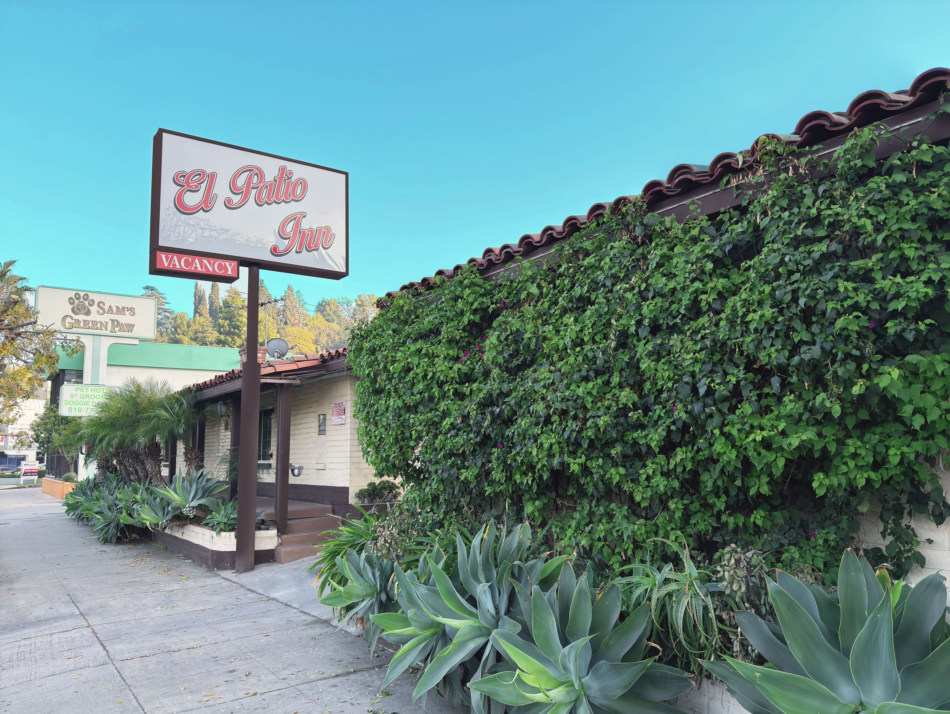 Um edifício com a placa 'El Patio Inn' e 'Sams Green Paw Pet Hotel'.