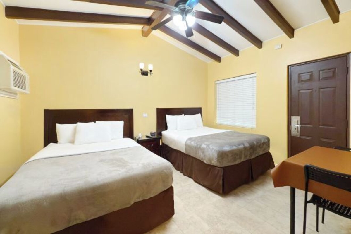 A hotel room with two beds, a ceiling fan, a table, and a door.