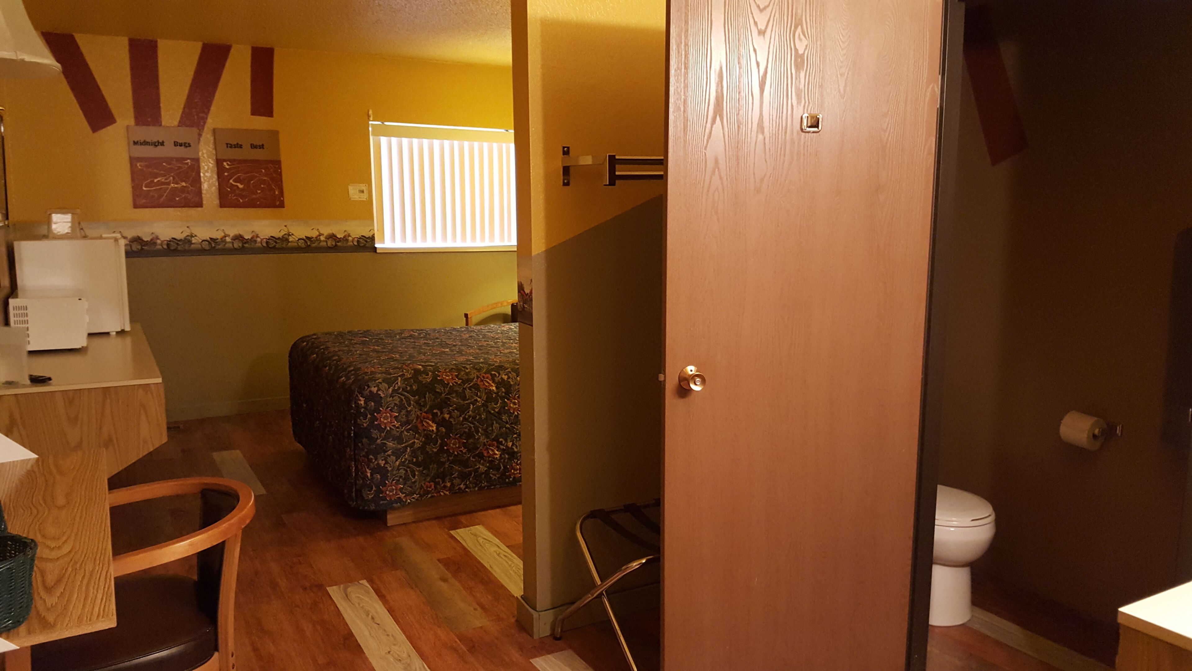 Una habitación con cama, escritorio, silla, inodoro y puerta.