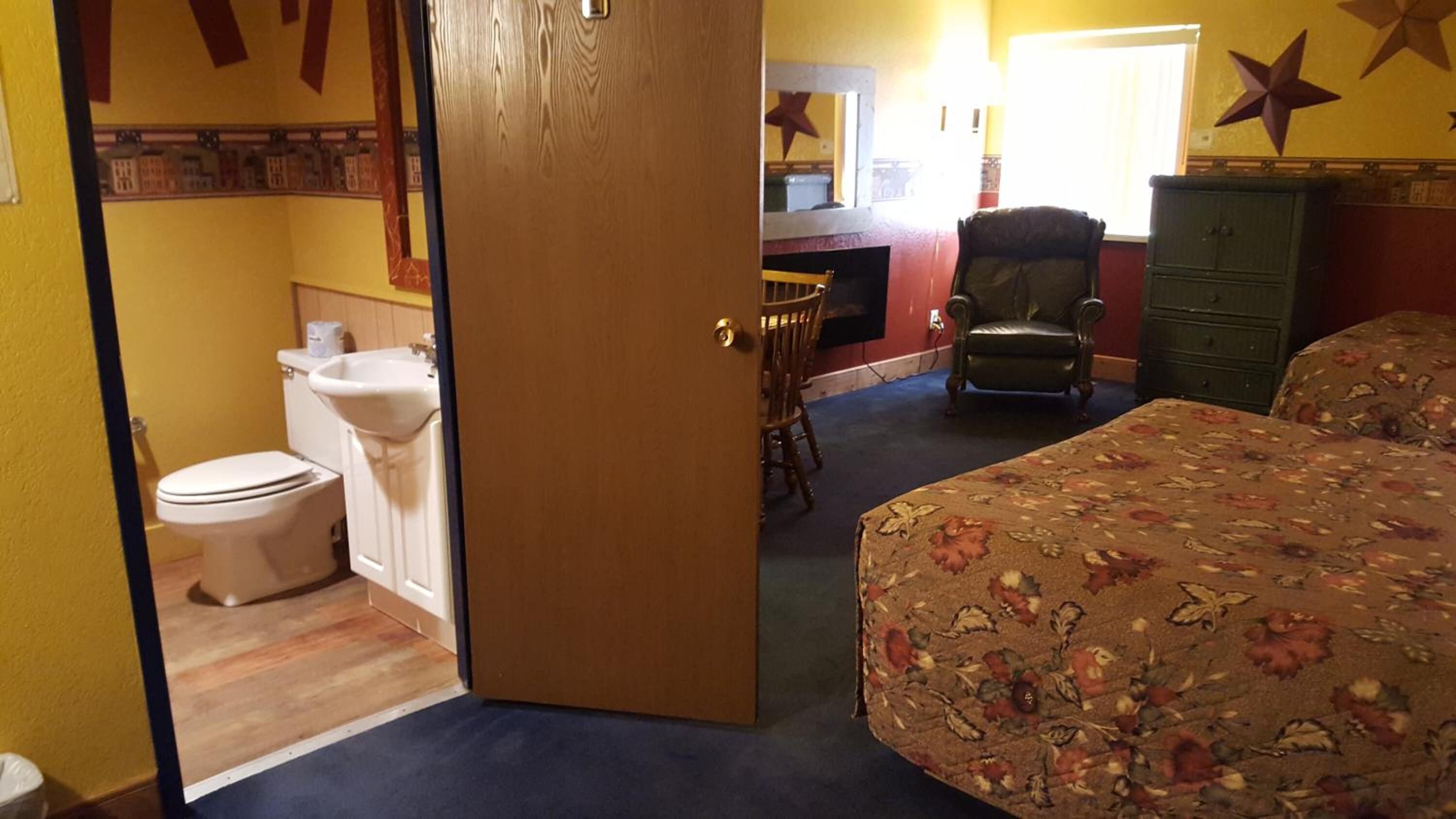 Ein Hotelzimmer mit Bett, Sessel, Kommode, Badezimmer mit Toilette und Waschbecken sowie Spiegel.
