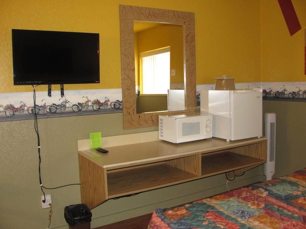 A room with a bed, a desk with a computer, a microwave, a refrigerator, and a TV mounted on the wall.