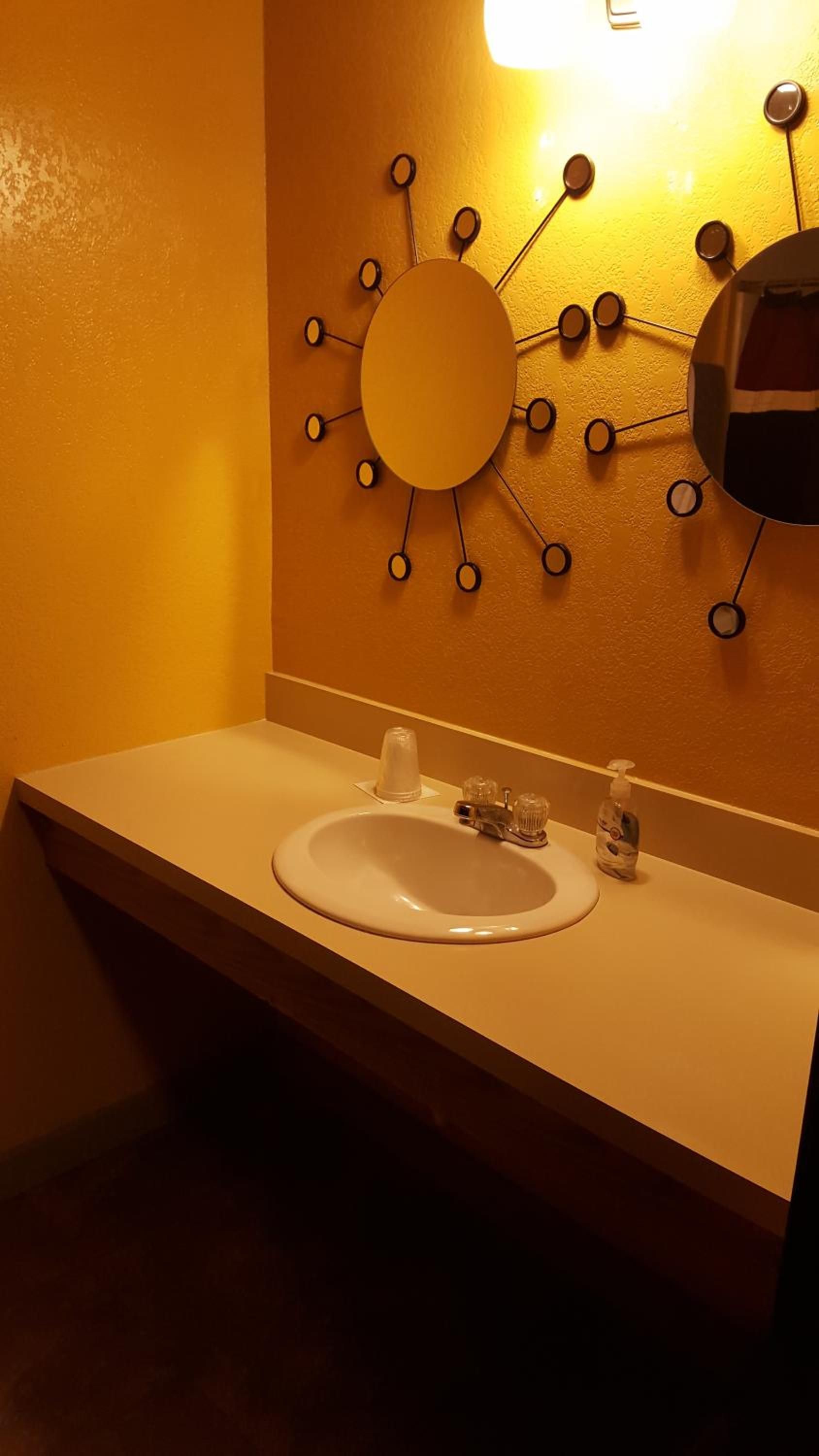 A bathroom with a sink, a mirror, and a wall-mounted light fixture.