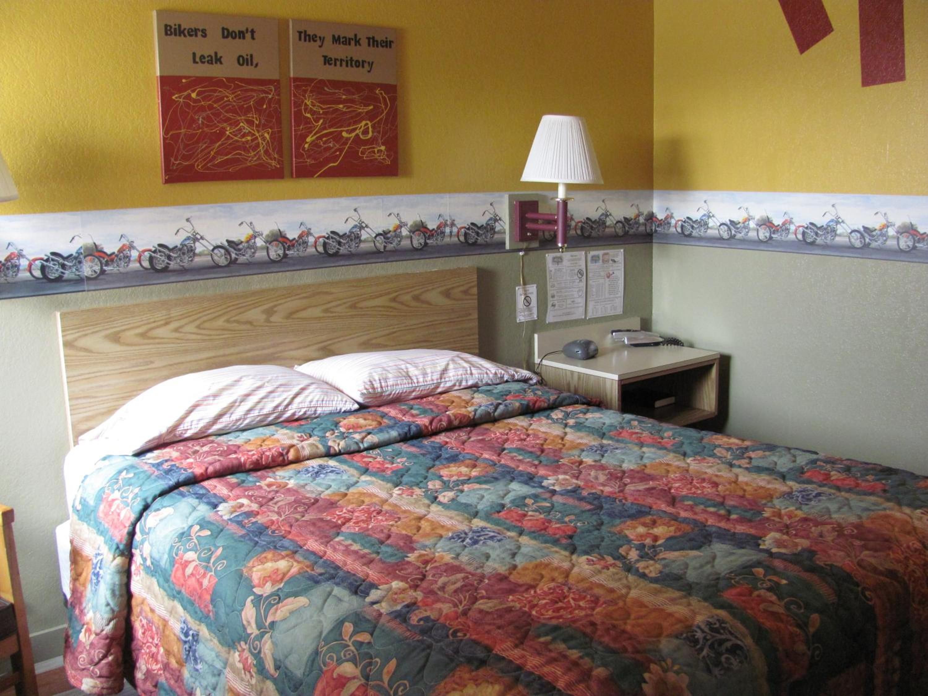 Una cama con colcha estampada, una mesita de noche con lámpara y cuadros con motocicletas.