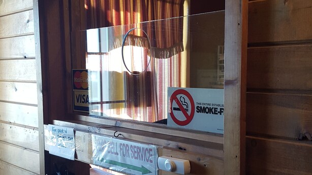 A check-in desk with a wooden interior, a window with curtains, a no-smoking sign, and a sign indicating the desk is for check-in. - Earth Inn Motel (Jackson)