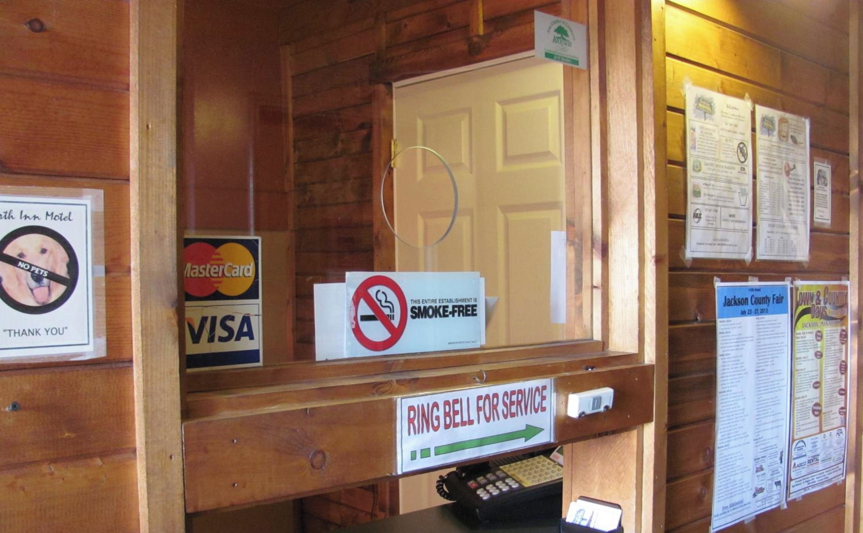 Un mostrador de recepción de madera con un cartel de 'No se admiten mascotas', un cartel de 'Gracias', un cartel de 'No fumar', un cartel de 'Tocar el timbre para asistencia' y un cartel promocional de la 'Jackson County Fair'.