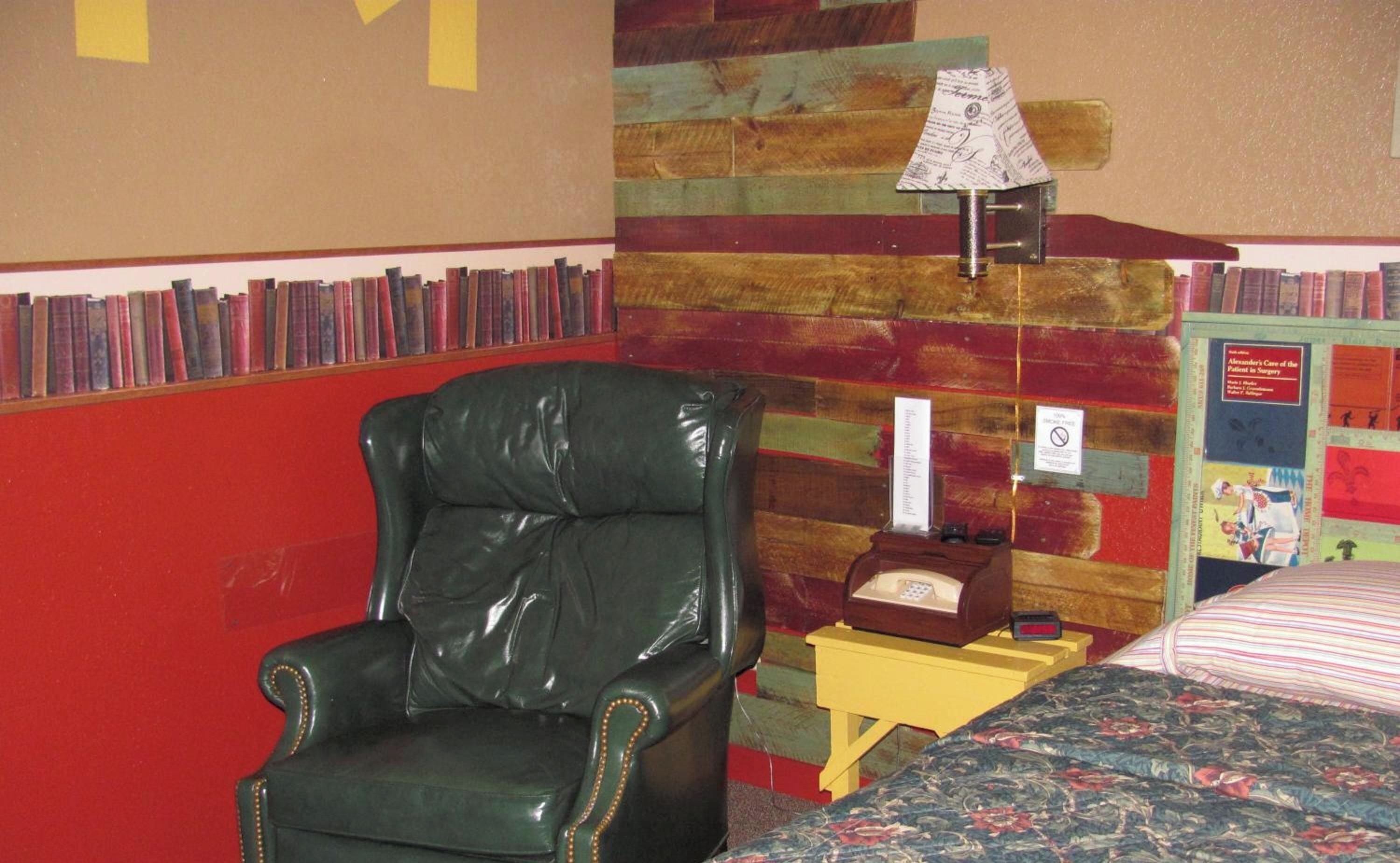 Una habitación con un sillón de cuero, una cama con colcha estampada y una pared con paneles de madera en tonos rojo y verde.