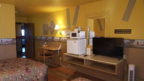 A hotel room with a bed, a desk, a microwave, a refrigerator, a television, and a wall-mounted mirror. - Earth Inn Motel (Jackson)