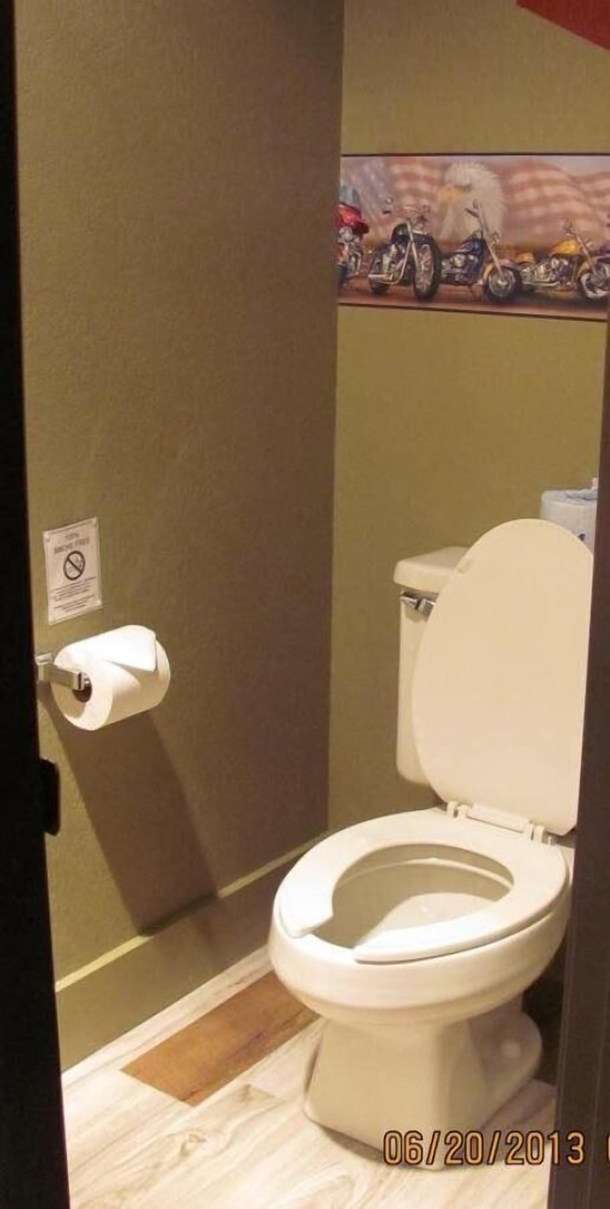Een kleine, privé badkamer met toilet, een rol toiletpapier en een bordje met de tekst rookverbod.
