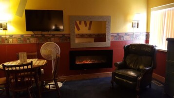 Quarto com televisão, lareira, poltrona de couro e mesa com cadeiras.