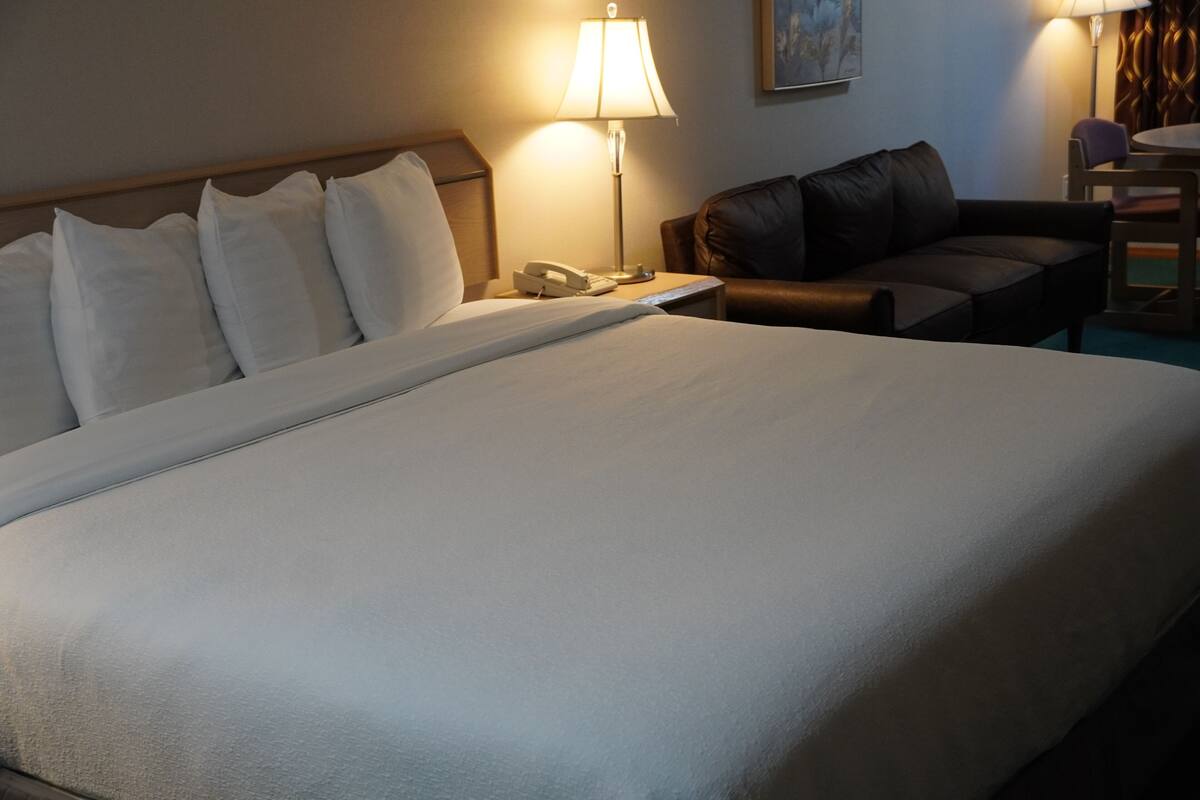A hotel room with a large bed, a bedside lamp, a telephone, a leather sofa, and a small table.