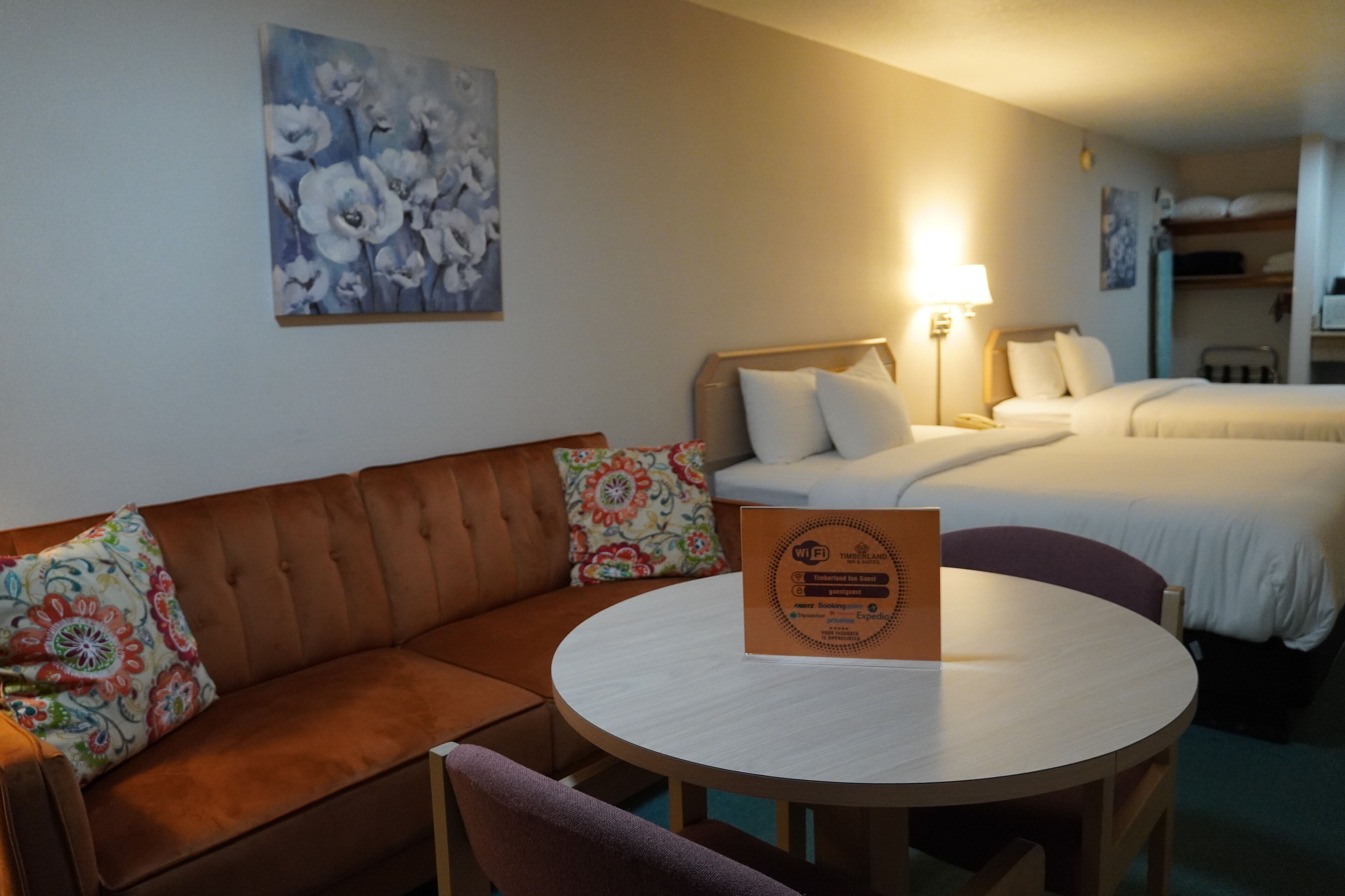 A hotel room with a brown sofa, a round table, and two beds. A sign on the table indicates WiFi availability.