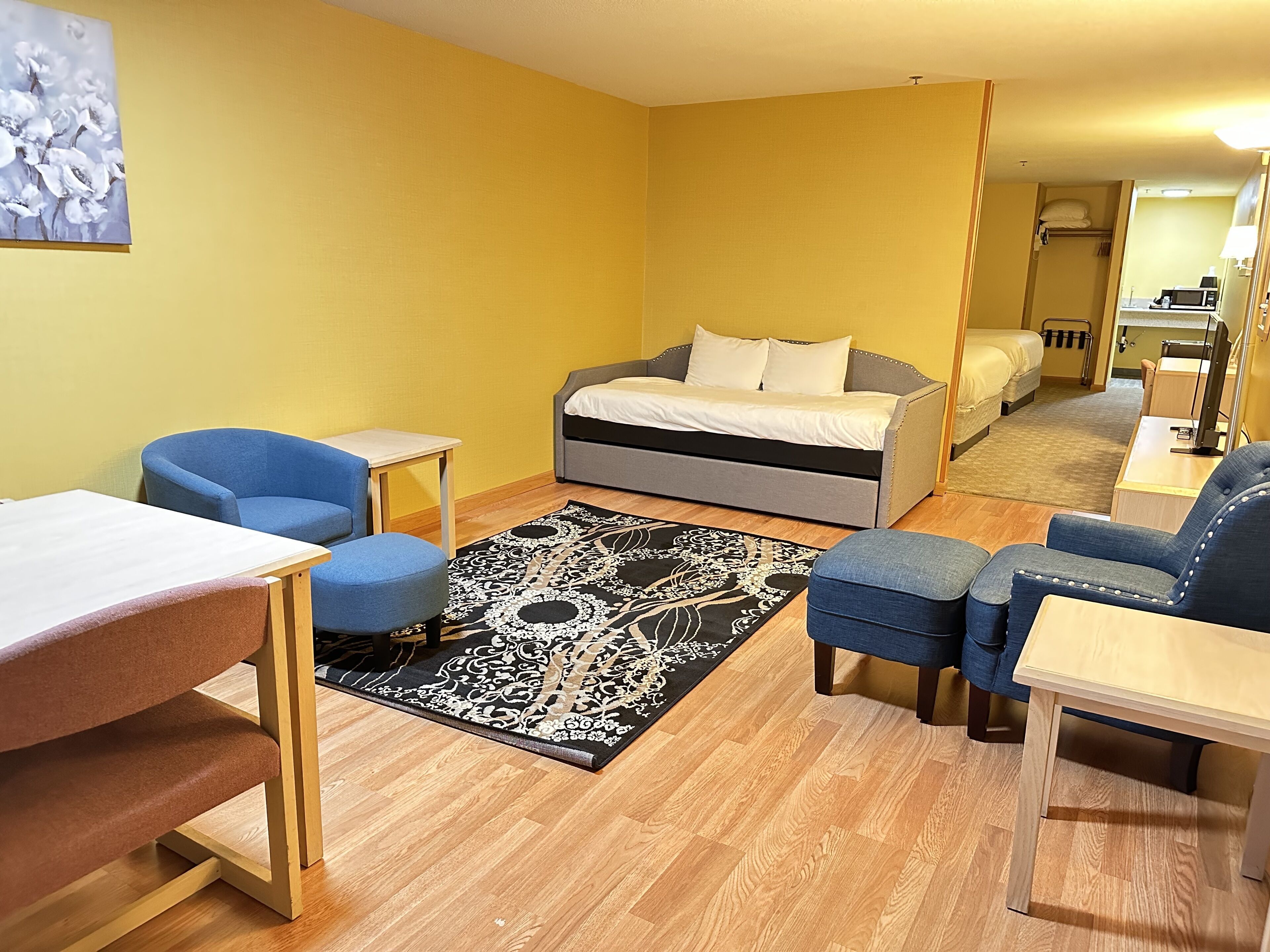 Habitación de hotel compacta con una cama, dos sillones azules, una mesita y una alfombra estampada.