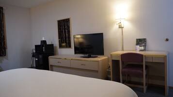 Ett hotellrum med en säng, ett skrivbord med en stol, en tv och en lampa.
