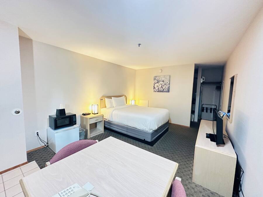 A hotel room with a single bed, bedside tables, a desk with a telephone, a microwave, and a small cabinet.