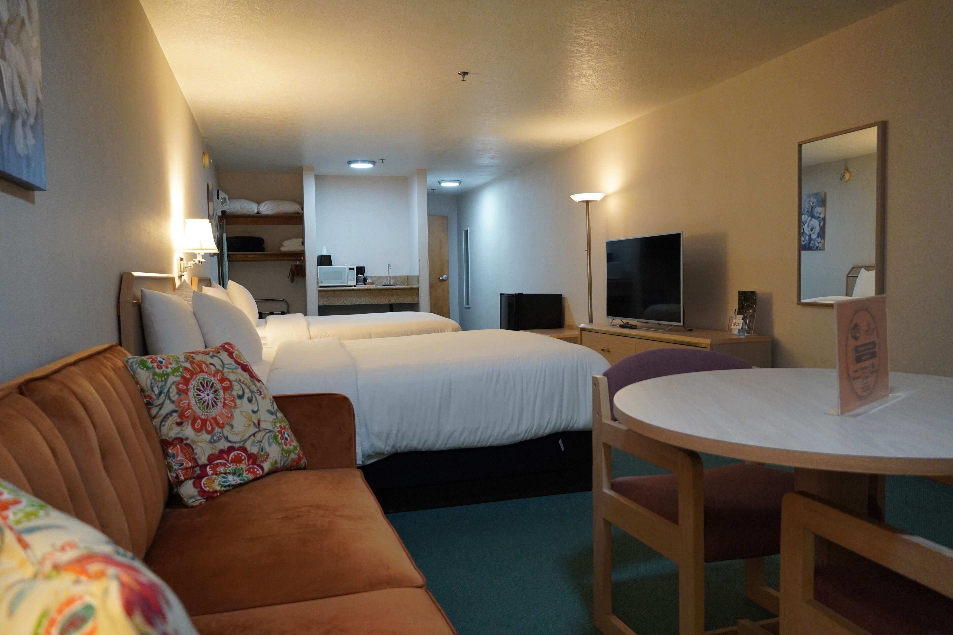 A hotel room with a bed, a sofa, a desk with a chair, a television, and a mirror.
