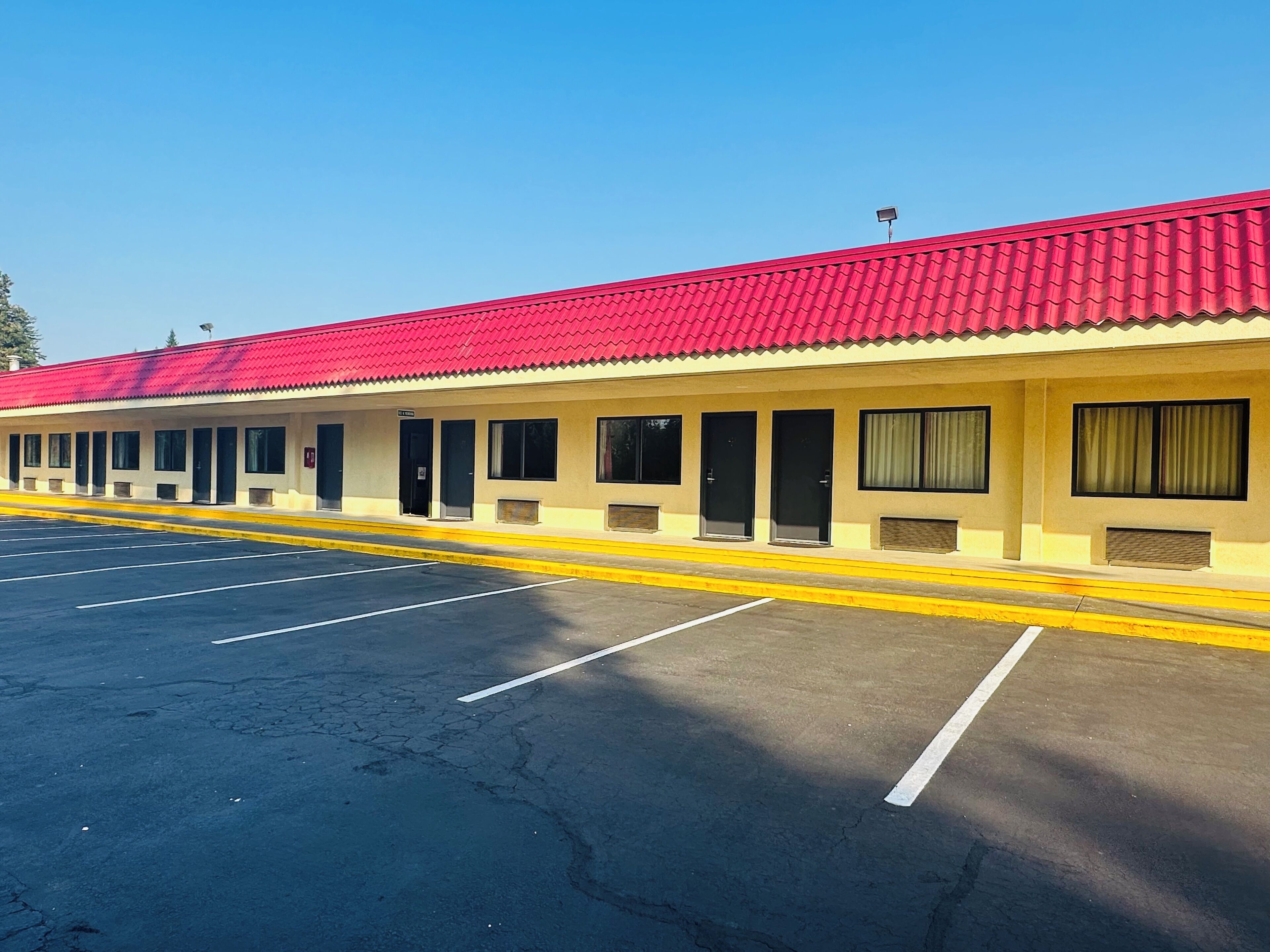 A motel with a red roof, multiple rooms with black doors, and a parking lot.