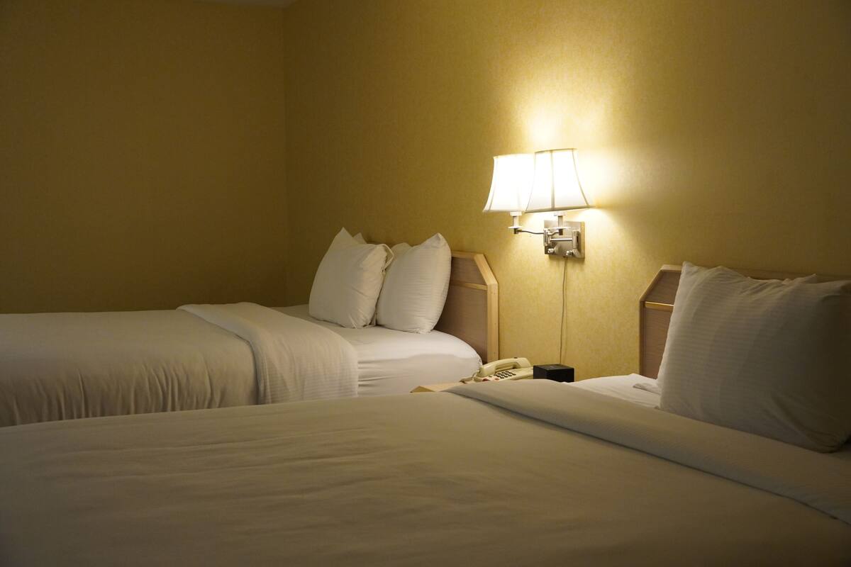 A hotel room with two beds, a bedside lamp, and a telephone.