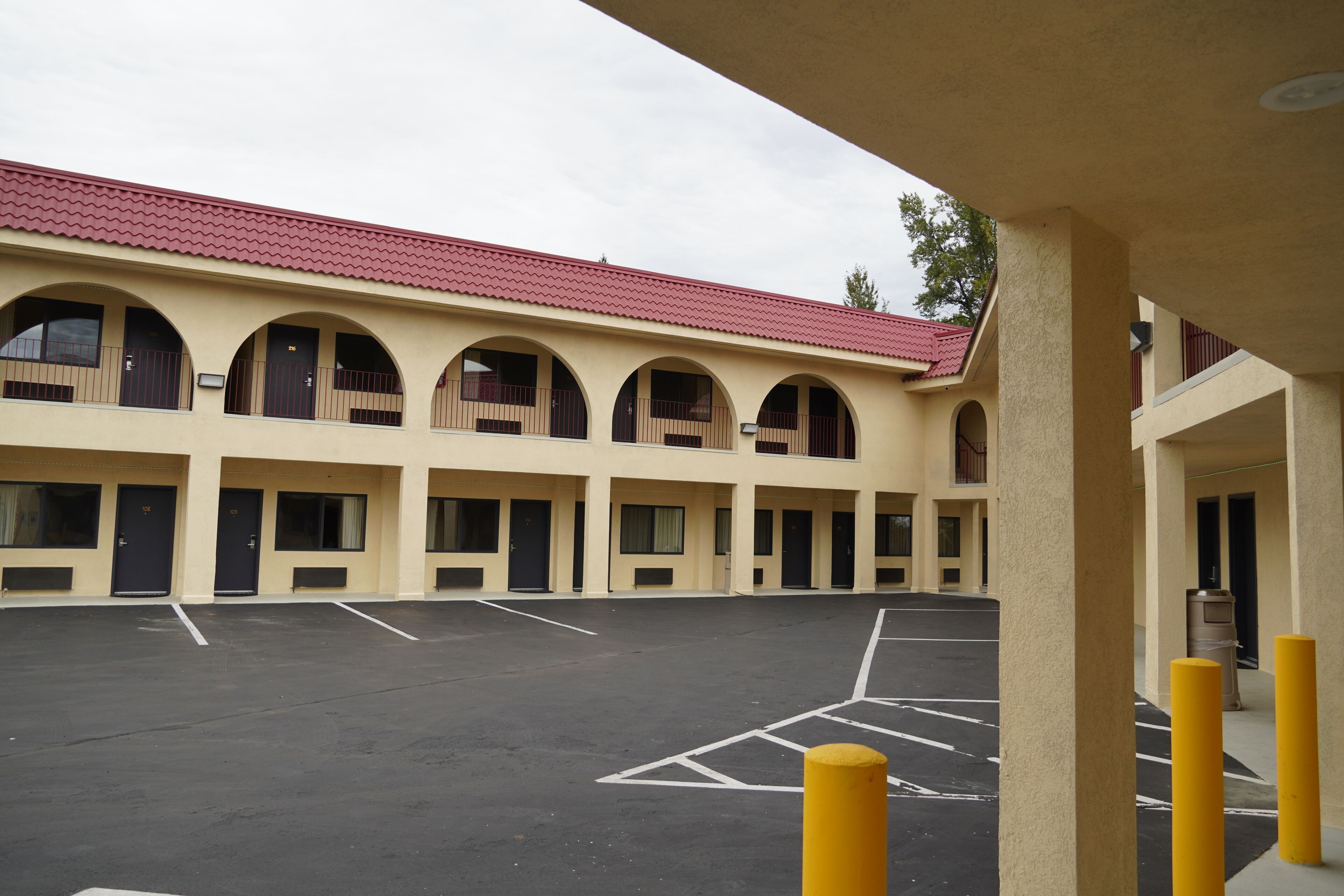 A building with multiple arched windows and doors, a parking lot with marked spaces, and a red-tiled roof.