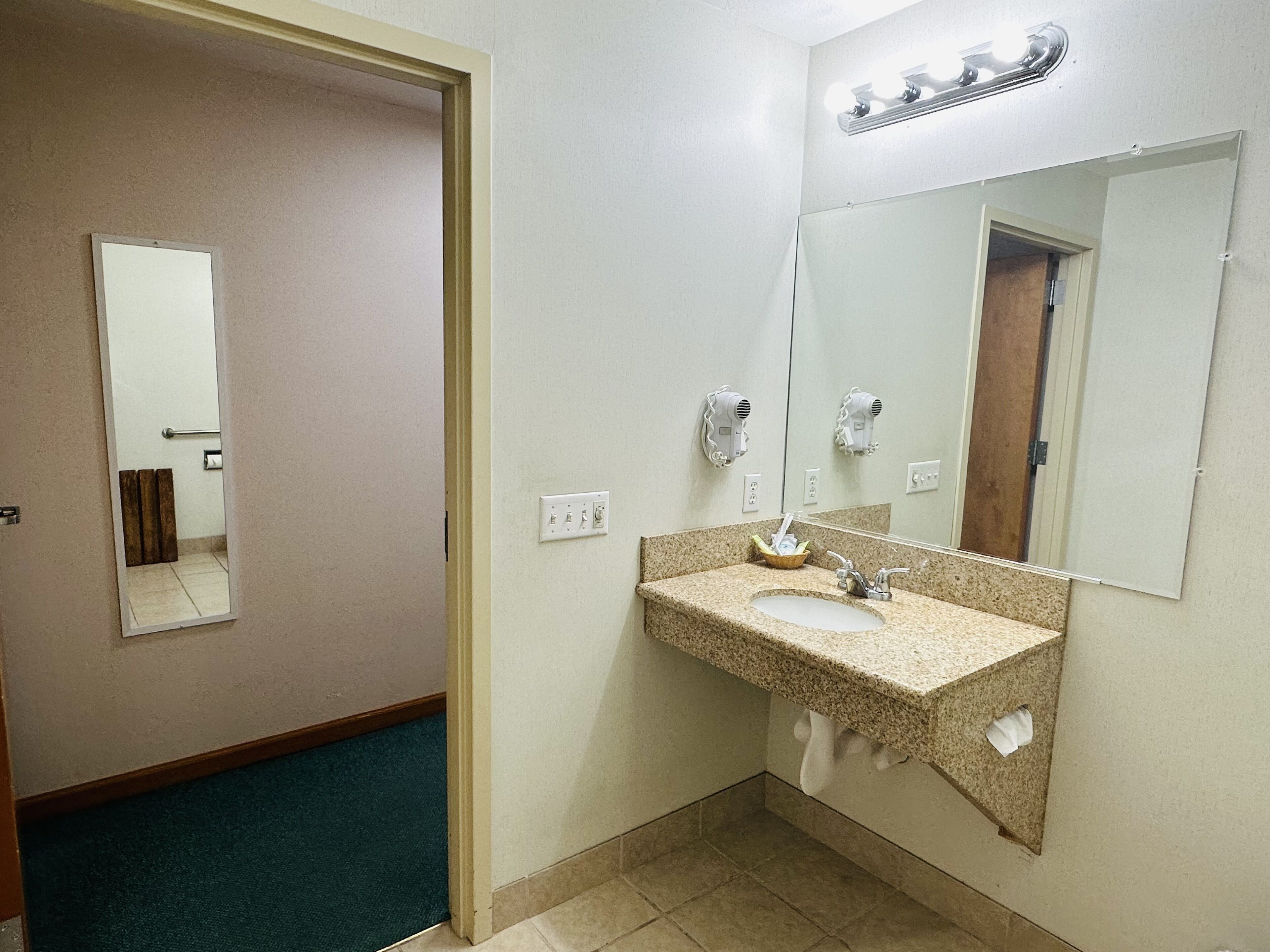 A hotel bathroom with a sink, mirror, towel rack, and hair dryer.