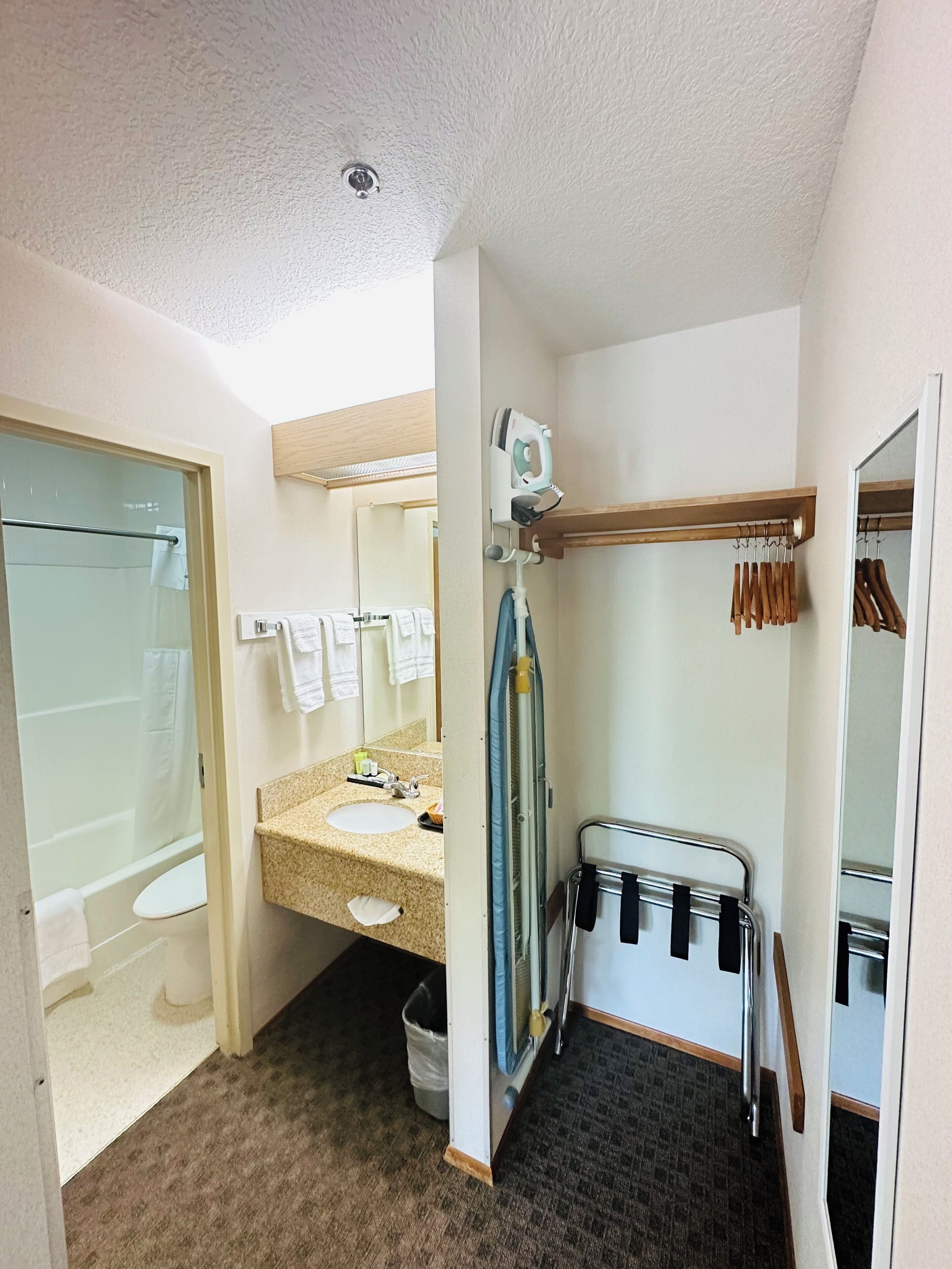 A bathroom with a sink, mirror, towel rack, shower, and a towel dispenser.